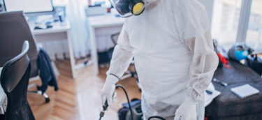 Man in protective suit disinfecting office work space